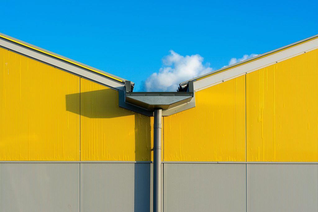 Close-up of a vibrant yellow industrial building exterior against a clear blue sky.